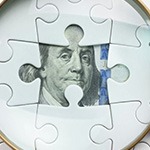 Magnifying glass examining money hidden behind a puzzle