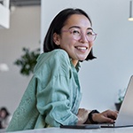 Woman with glasses smiling while working on laptop