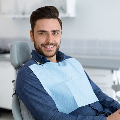 Man smiling in dental chair with hands folded