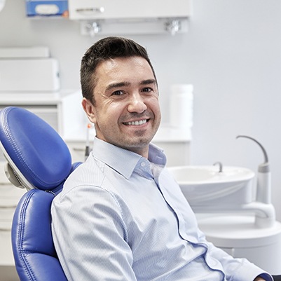 Man sitting in dental chair smiling after smile makeover in Frisco, TX