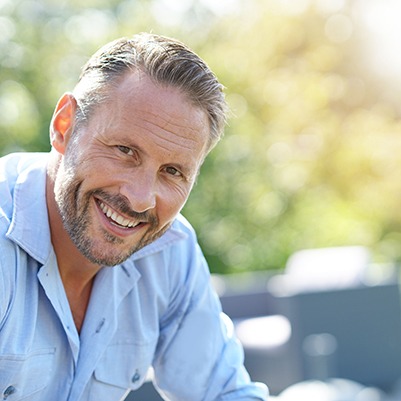 Older man sitting down outside and smiling