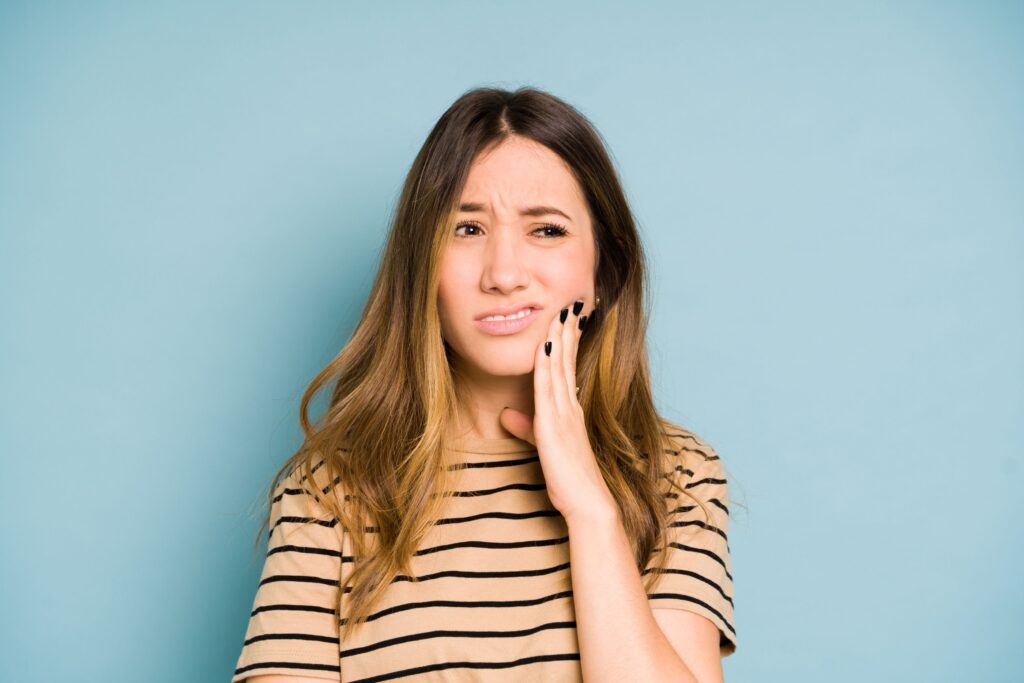 Woman in striped shirt pressing hand to jaw in pain